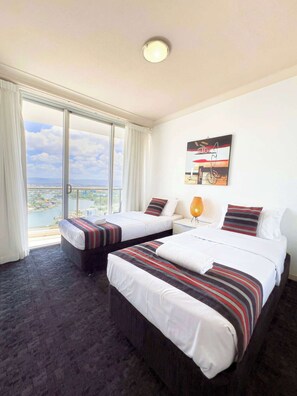 A hotel room with two beds, a large window with a view of a cityscape, and a ceiling light. - 26th Floor at Chevron (Surfers Paradise)