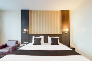 A hotel room with a large bed, two bedside lamps, a telephone, and a leather armchair. - Collection O Stefani City Hotel (Pekanbaru)