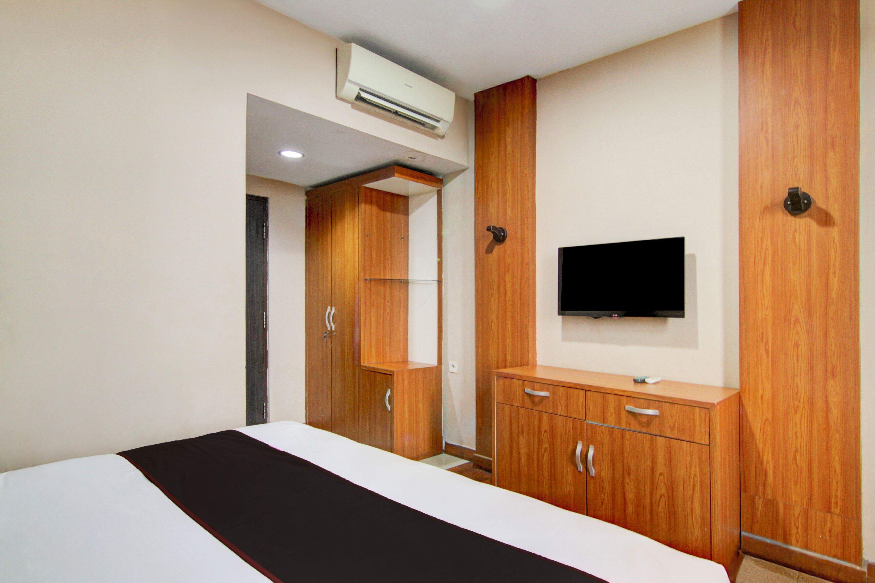 Quarto de hotel com cama, guarda-roupa de madeira, televisão na parede e aparelho de ar condicionado.