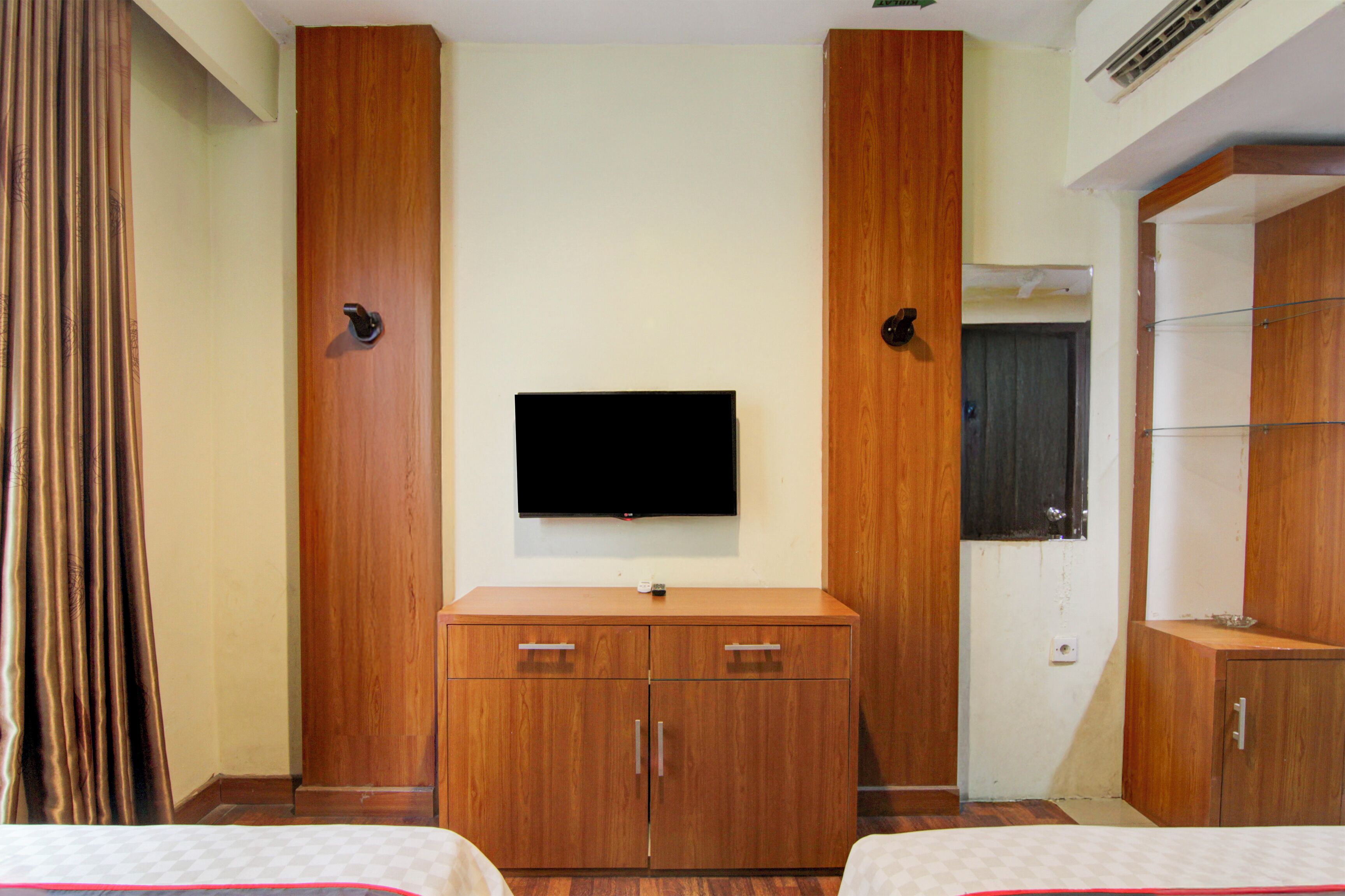 A hotel room with a wooden wardrobe, a flat-screen TV mounted on the wall, and a bed with a checkered bedspread.