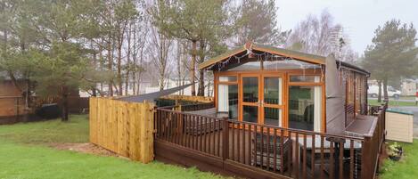 A wooden cabin with a deck, large windows, and a fenced yard.
