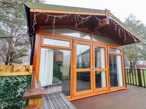 Une structure en bois dotée de grandes portes vitrées et d’une terrasse en bois.