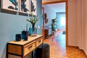 Ein Flur mit Holzboden, einem Schreibtisch mit Schubladen, einer Vase mit Blumen und gerahmten Kunstwerken an der Wand.