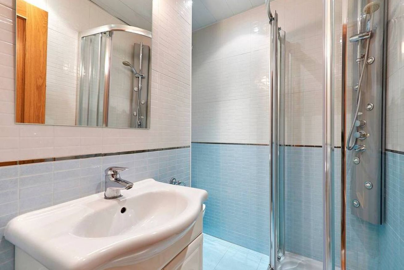 Un baño con lavamanos blanco, espejo y ducha con mampara de vidrio.