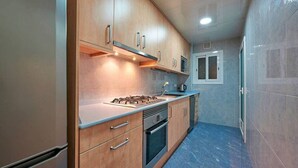 A compact kitchen with wooden cabinets, a gas stove, an oven, and a microwave. - Design Flat, Terrace / Paseo de Gracia, Born (Barcelona)
