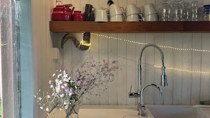 Eine Küche mit weißer Arbeitsplatte, einem Spülbecken, einer Pendelleuchte, einem Regal mit Küchenutensilien und einer Vase mit Blumen.