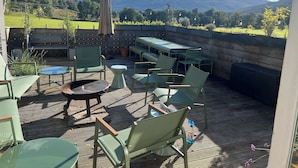 Eine Terrassengaststätte mit grünen Stühlen und Tischen, einem Grill und Blick auf eine Berglandschaft.