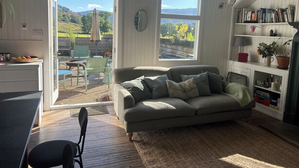 Ein gemütliches Wohnzimmer mit einer Couch, einem Bücherregal und Blick ins Freie.