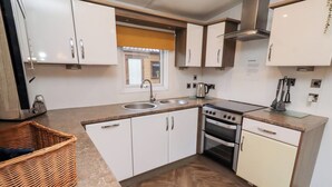 Una cocina compacta con armarios blancos, estufa, pileta y piso de madera con diseño en espiga.
