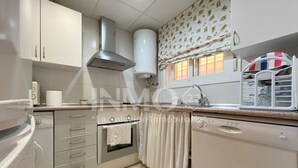 Una cocina compacta con armarios blancos, una campana extractora de acero inoxidable, horno integrado y lavavajillas.