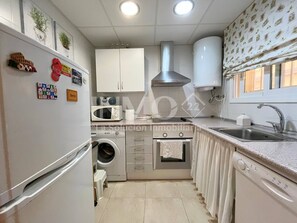 A compact kitchen with a washing machine, microwave, and a stove. - Ground floor flat in 2nd line beach, terrace (Cambrils)