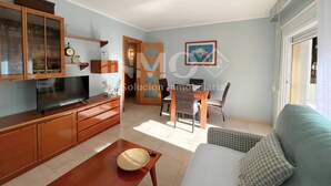 Una sala de estar con televisor, armarios de madera, una mesa de comedor con sillas y un sofá.