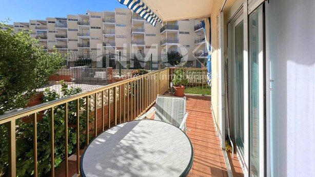 Un balcón con mesa y sillas, una planta en maceta y vistas a edificios de apartamentos.