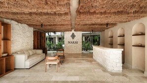 A lobby with a stone wall, a reception desk, a sofa, chairs, and a ceiling with a thatched design. - Narai Solecito House Tulum Jungle Views Aldea Zama (Tulum)