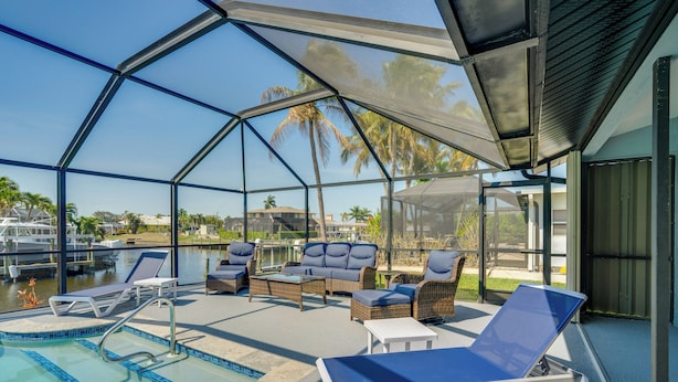 A glass-enclosed pool area with lounge chairs, a sofa, and a small table. - Luxe Waterfront Cape Coral Home w/ Gulf Access! (Cape Coral)