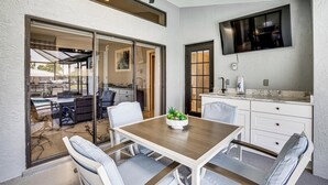 An open-plan living and dining area with a ceiling fan, a TV mounted on the wall, and a view into the adjacent kitchen. - Luxe Waterfront Cape Coral Home w/ Gulf Access! (Cape Coral)