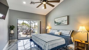 A bedroom with a large bed, a ceiling fan, a view through a glass door, and a nightstand with a lamp. - Luxe Waterfront Cape Coral Home w/ Gulf Access! (Cape Coral)