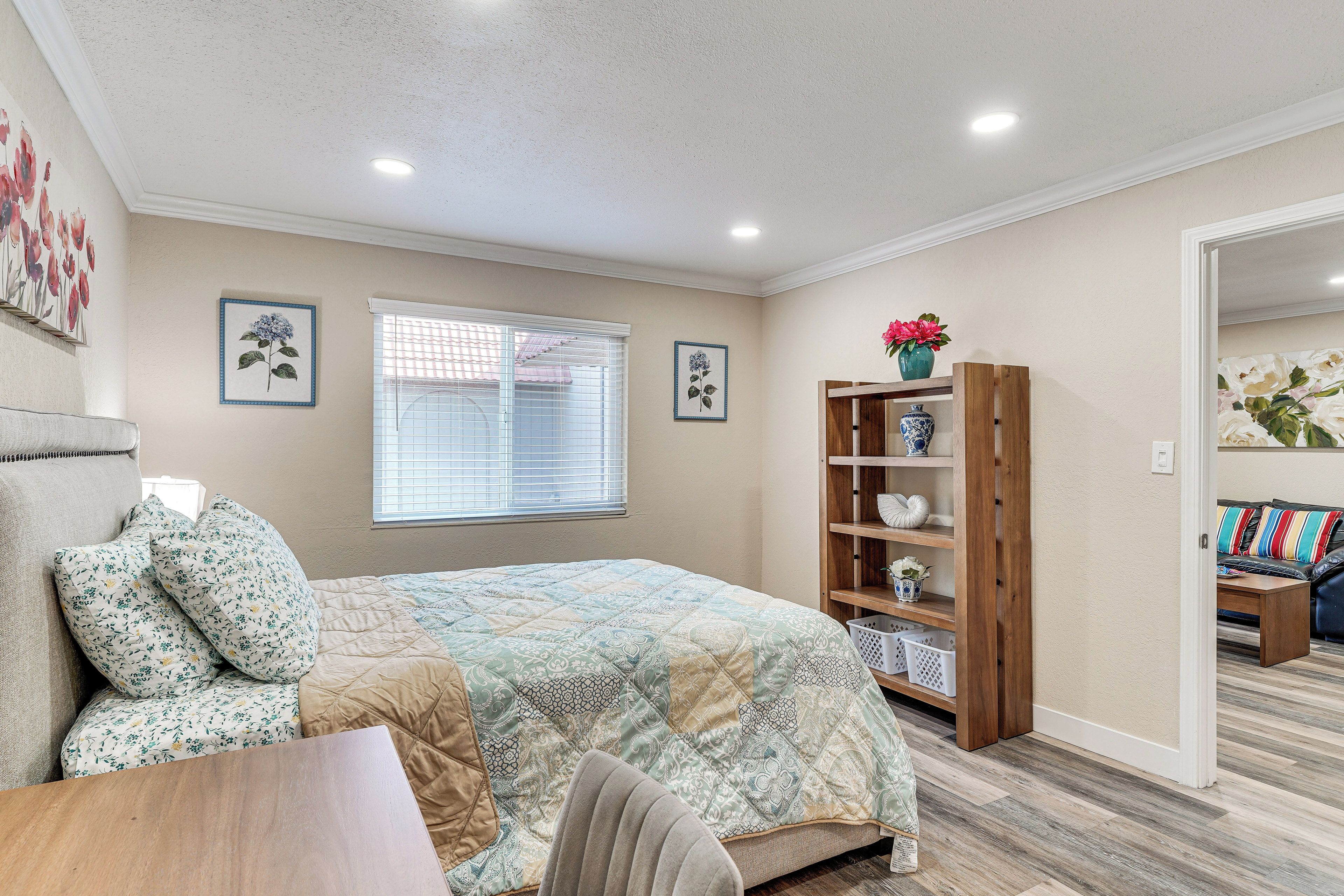 A bedroom with a bed, a wooden nightstand, a chair, a window with blinds, and a bookshelf.