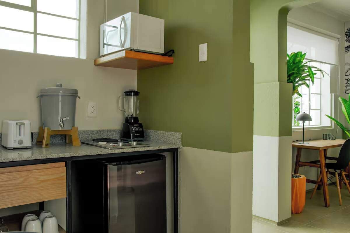 A compact kitchen with a refrigerator, toaster, blender, and a coffee maker on the countertop.