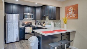 A modern kitchen with dark cabinets, stainless steel appliances, a white countertop island, and a painting of flowers on the wall. - 2 Mi to Dtwn Pleasanton Condo w/ Pool Access (Pleasanton)
