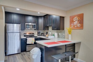 Una cocina moderna con armarios oscuros, electrodomésticos de acero inoxidable, una isla con encimera blanca y un cuadro de flores en la pared.