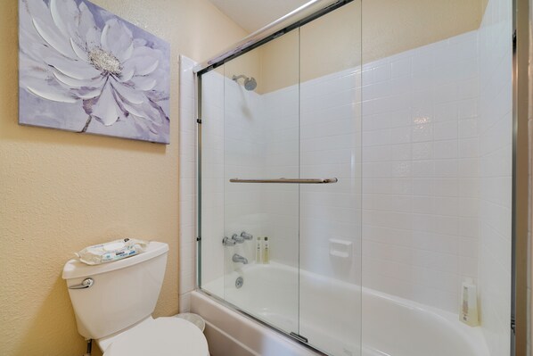 Une salle de bain avec une douche à parois de verre, des toilettes et une grande œuvre d’art à motifs floraux accrochée au mur.