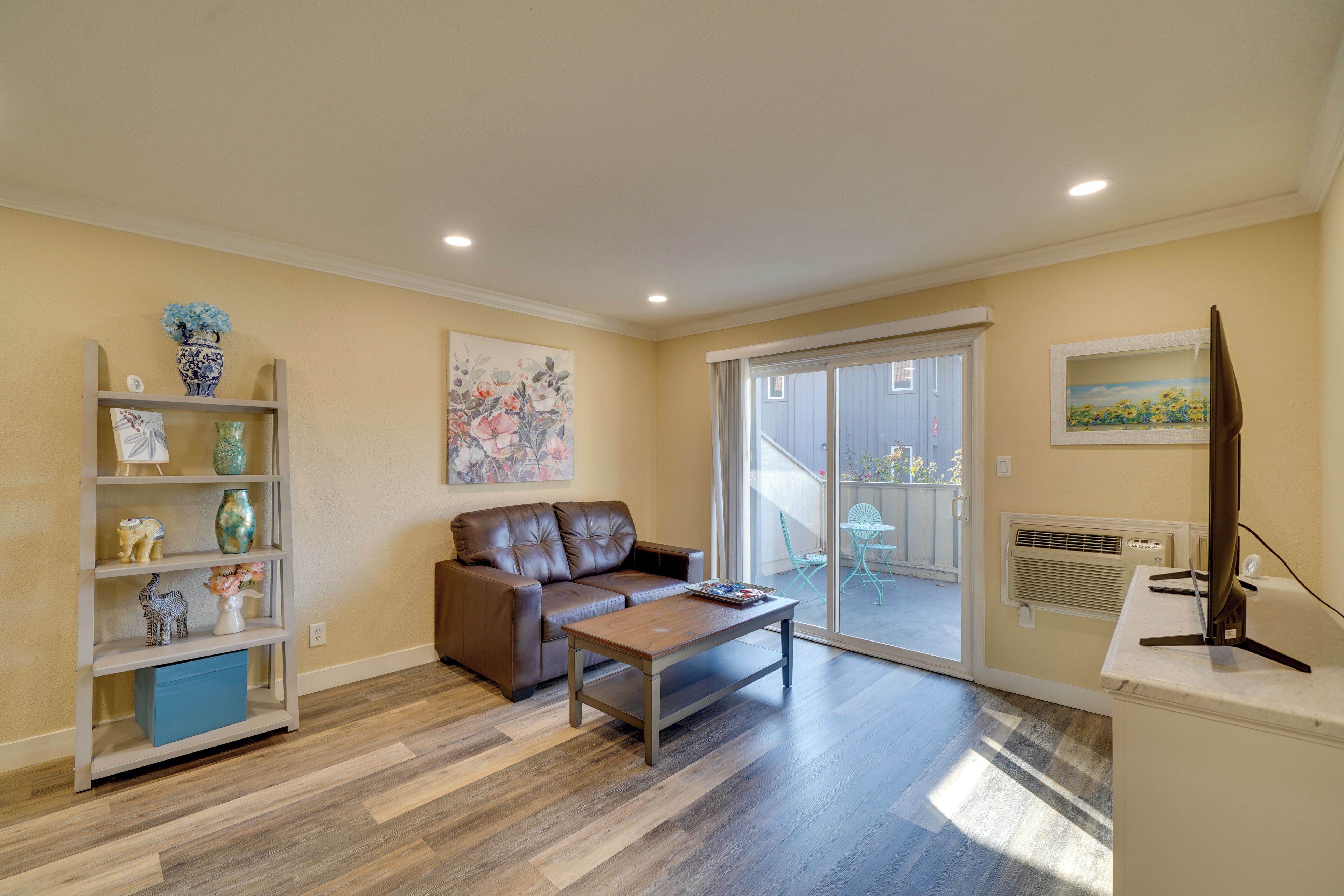 A living room with a brown leather sofa, a wooden coffee table, and a bookshelf with decorative items.