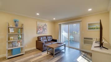 A living room with a brown leather sofa, a wooden coffee table, and a bookshelf with decorative items.