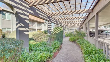 A covered walkway with a patterned ceiling, surrounded by greenery and a gravel path.
