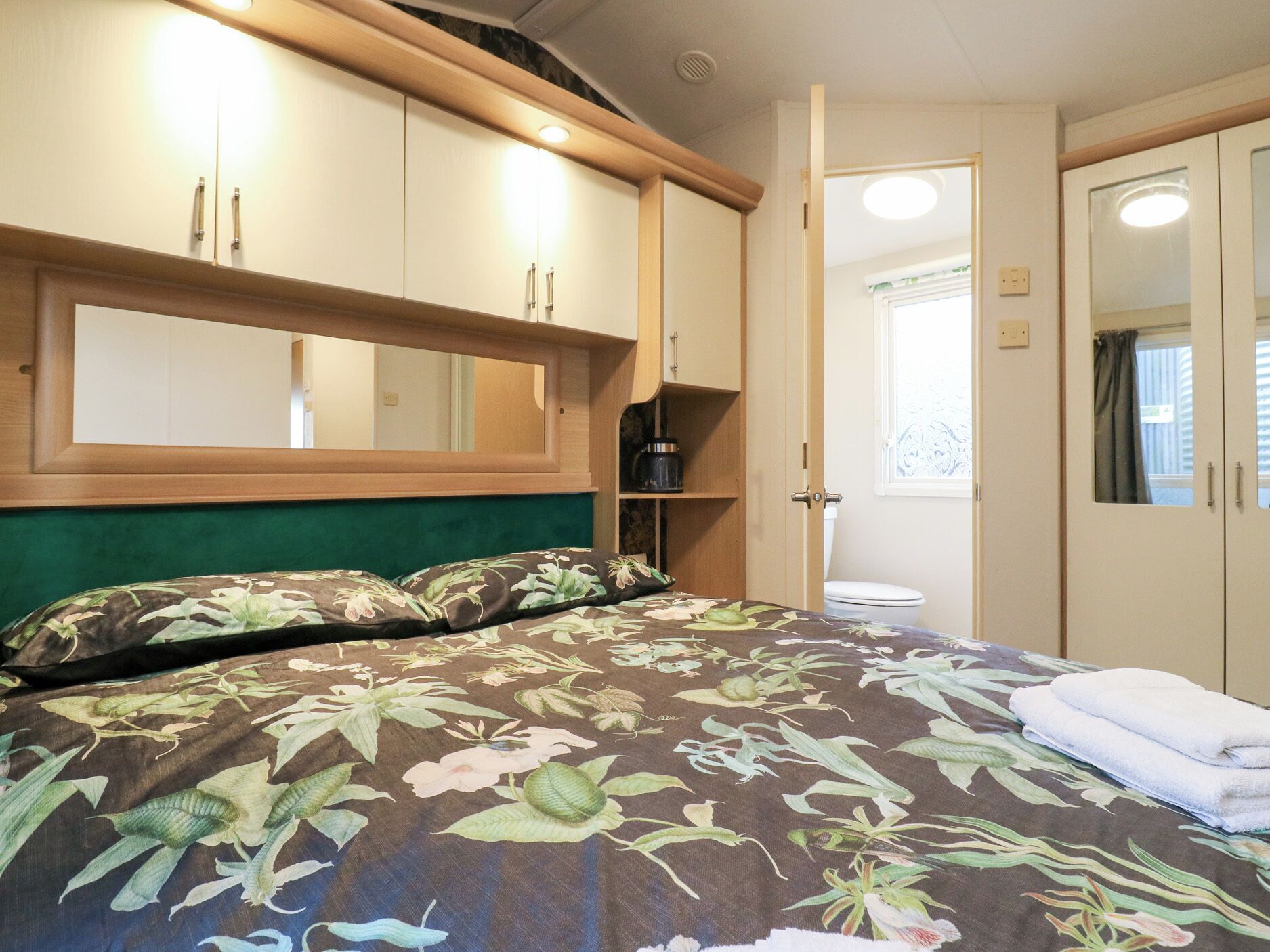 A bedroom with a bed, a mirror, a wardrobe, and a toilet.