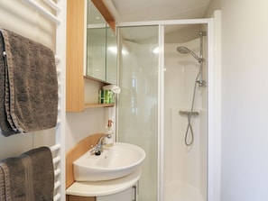 A bathroom with a white sink, a glass shower enclosure, and a towel rack with a brown towel. - Granada at Avalon Eco Farm (Cambridge)
