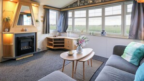 A cozy living room with a fireplace, a dining table, and a sofa. - Granada at Avalon Eco Farm (Cambridge)