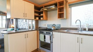 A compact kitchen with white cabinets, a stove, a sink, and a window with a view. - Granada at Avalon Eco Farm (Cambridge)