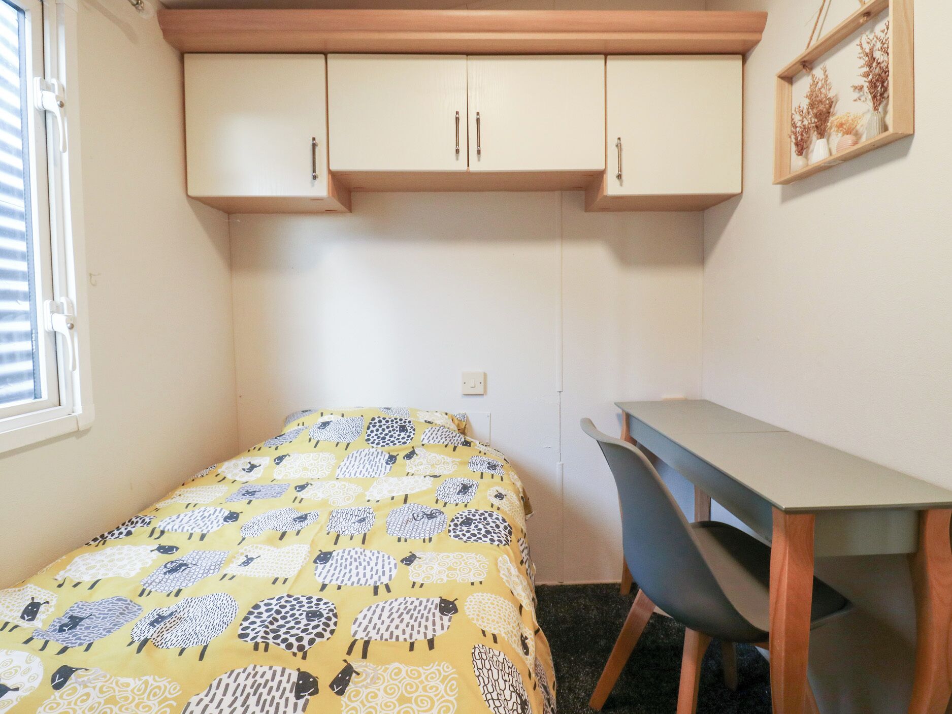 A small bedroom with a bed, a desk, and a window.