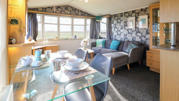 A cozy living room with a glass dining table, grey sofa, and wooden cabinets. - Granada at Avalon Eco Farm (Cambridge)