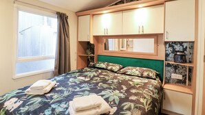 A bedroom with a bed, a window, curtains, and built-in wooden cabinets. - Granada at Avalon Eco Farm (Cambridge)