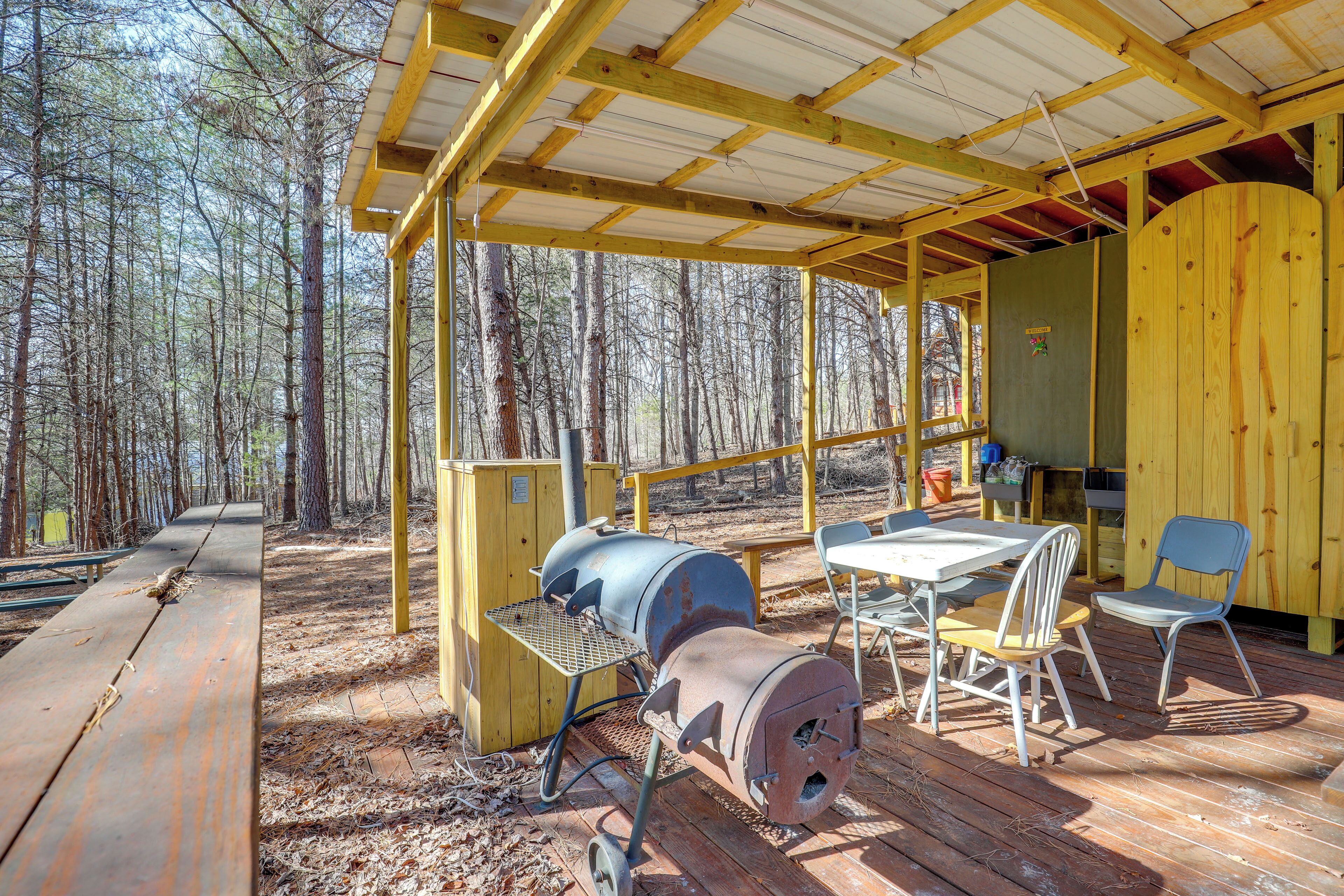 A covered outdoor area with a grill, picnic table, and chairs.