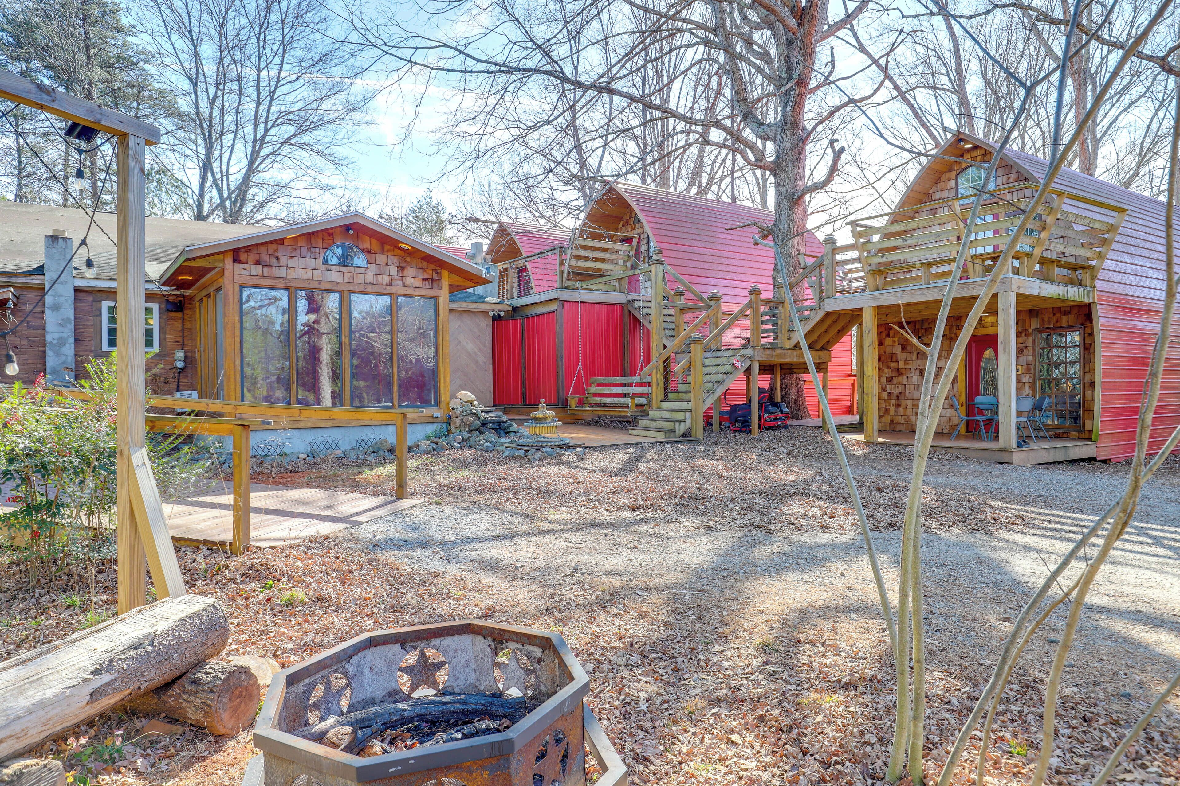 A rustic cabin with a red exterior, wooden deck, and a fire pit in the foreground.