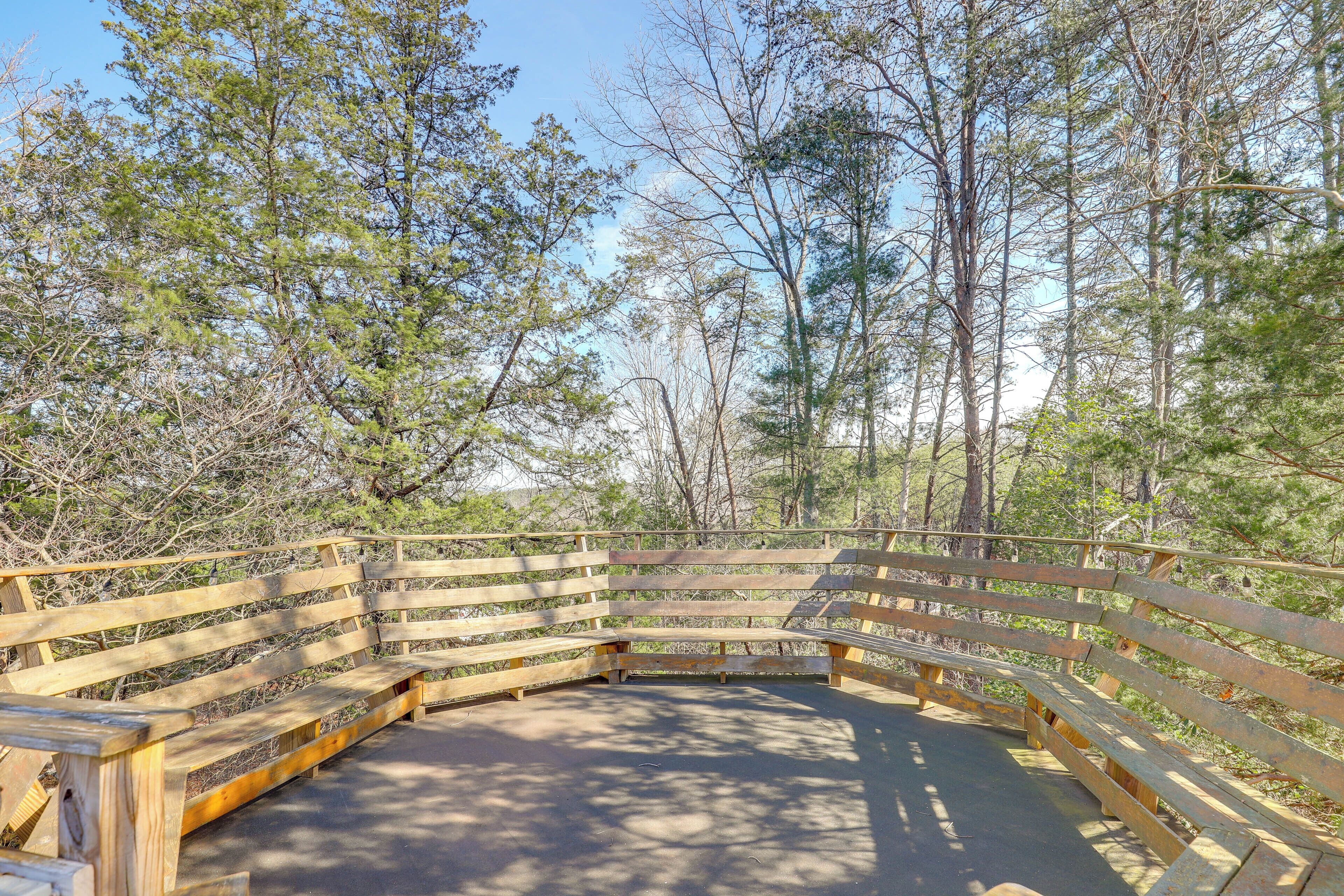 A wooden bench area with a curved railing, surrounded by trees.