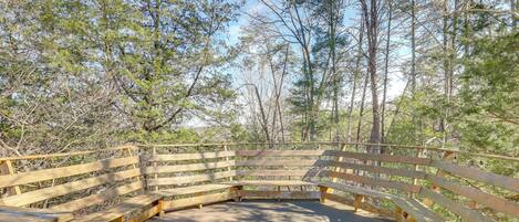 A wooden bench area with a curved railing, surrounded by trees.