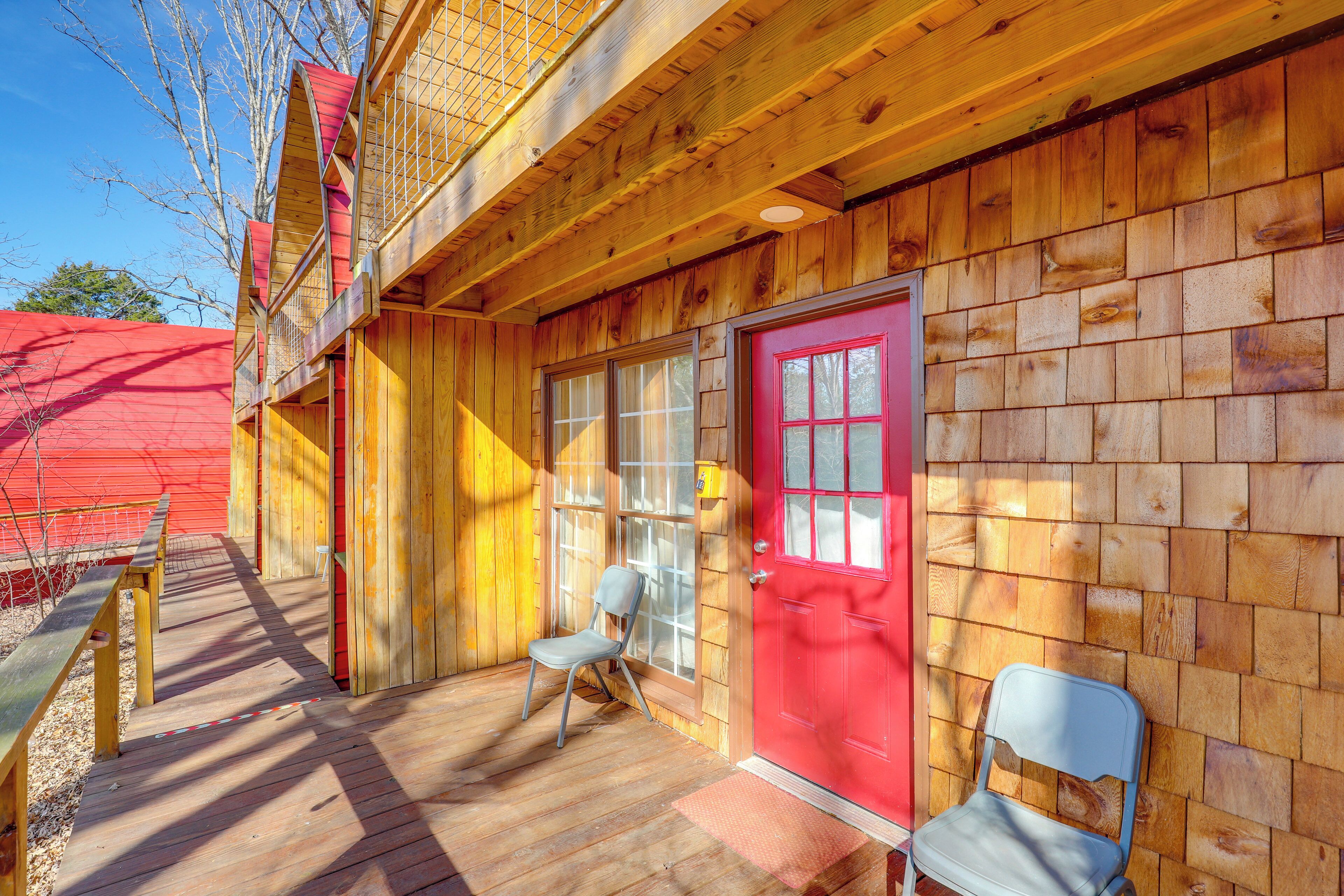 Une cabane en bois avec une porte rouge, deux chaises à l’extérieur et une terrasse en bois.
