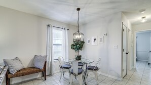 A dining area with a round table, four chairs, a bench with cushions, a hanging light fixture, and a window with curtains. - Visit Route 66! Pet-friendly Joplin Gem w/ Yard (Joplin)