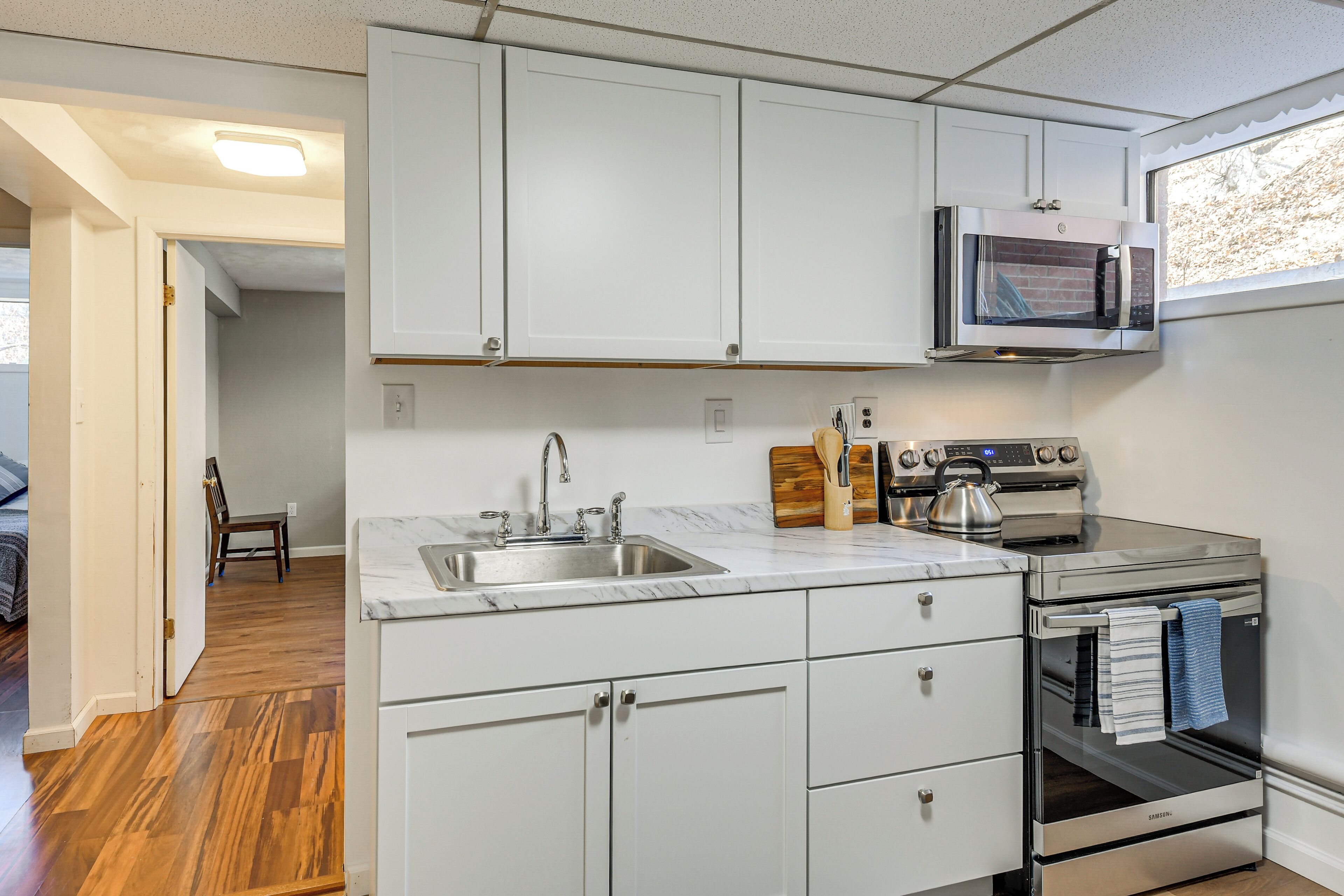 A kitchen with white cabinets, a stainless steel sink, a microwave, and an oven.
