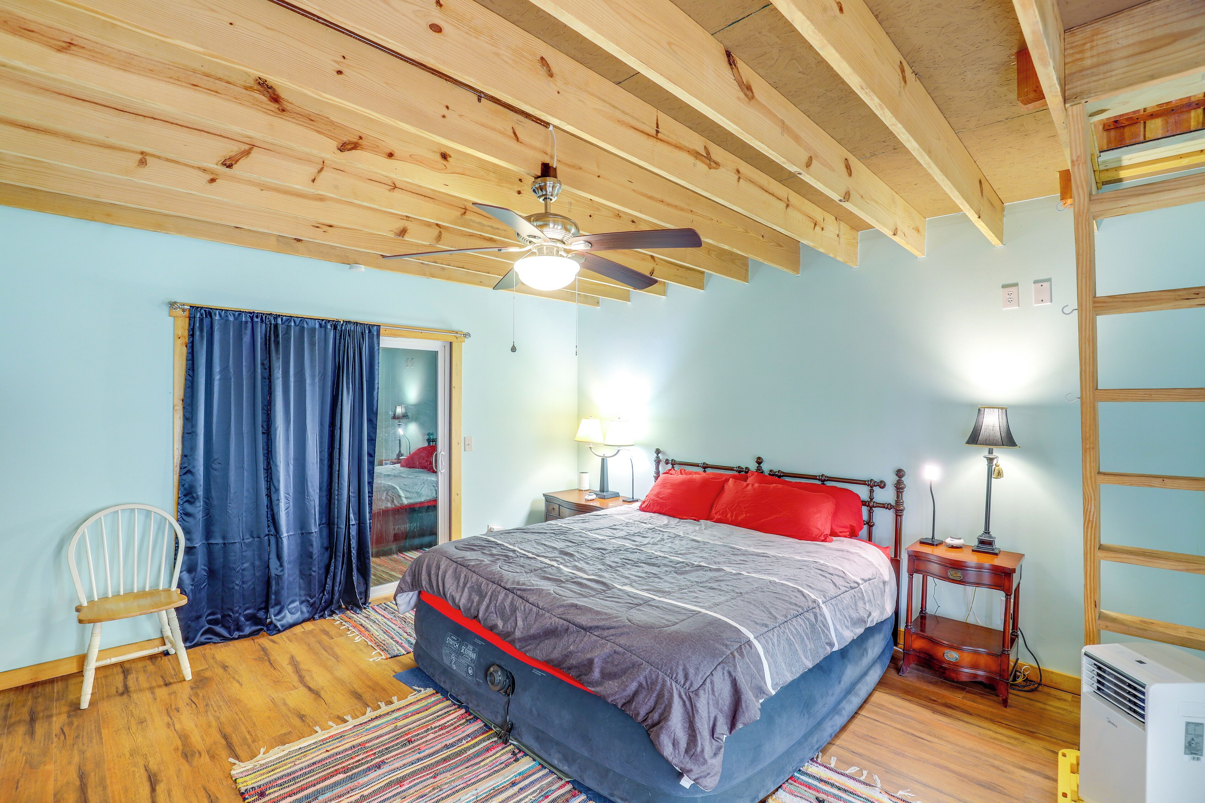A bedroom with a bed, a ceiling fan, a nightstand, a chair, and a window with curtains.