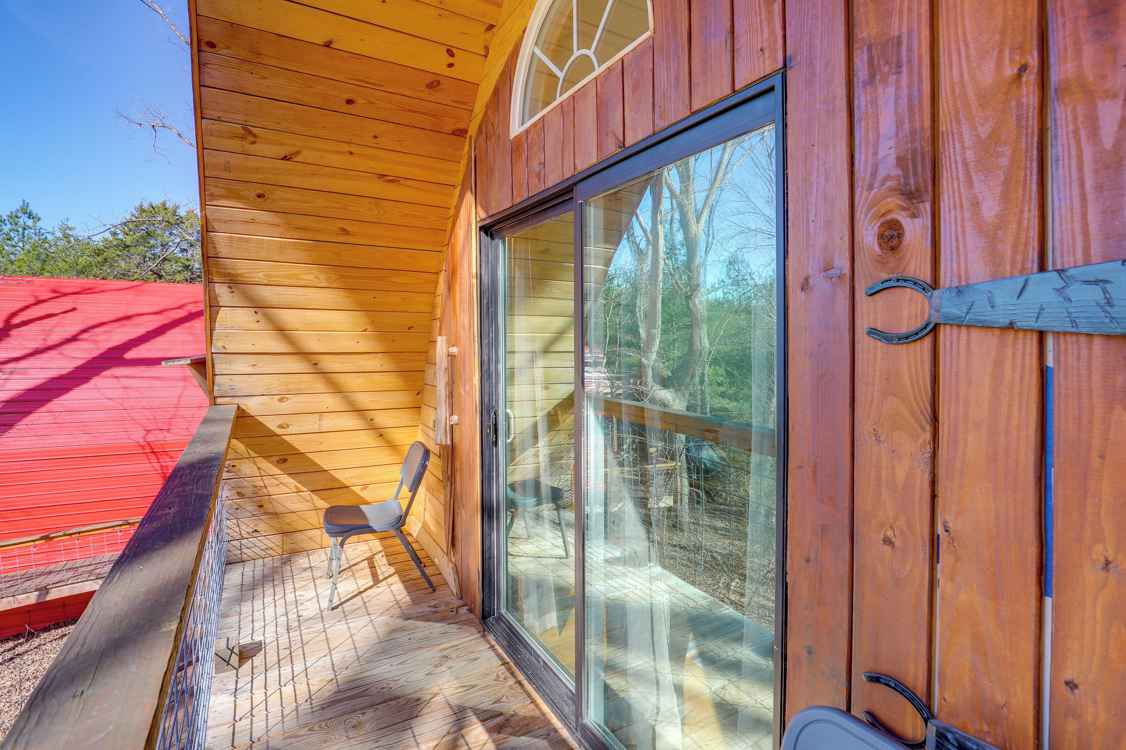 A wooden cabin with a large sliding glass door, a red roof, and a wooden deck.