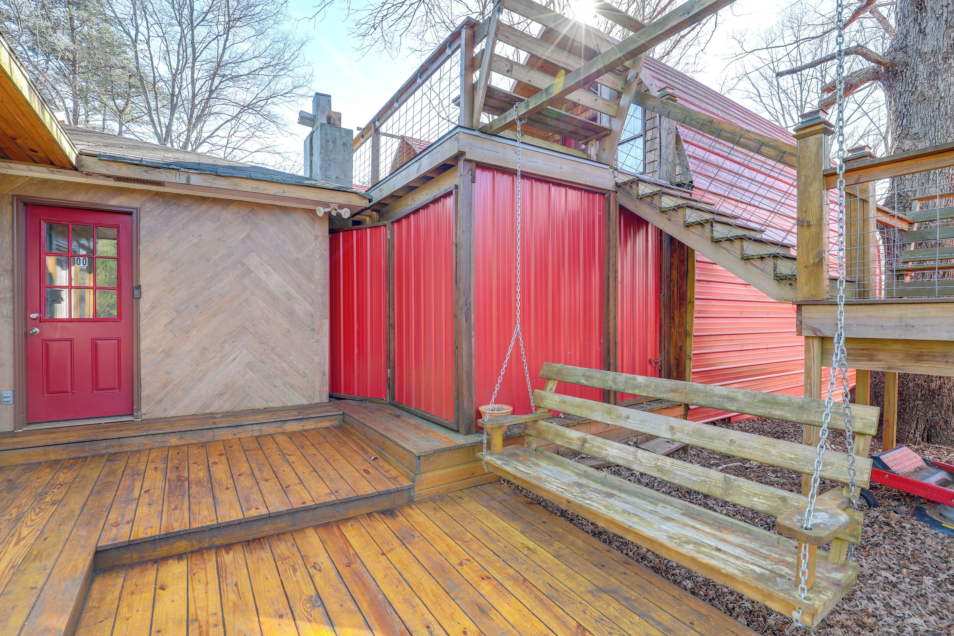 Une terrasse en bois avec une porte rouge, un banc en bois et un bâtiment rouge dont le mur est orné d’un motif en chevrons.