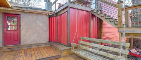 Une terrasse en bois avec une porte rouge, un banc en bois et un bâtiment rouge dont le mur est orné d’un motif en chevrons.