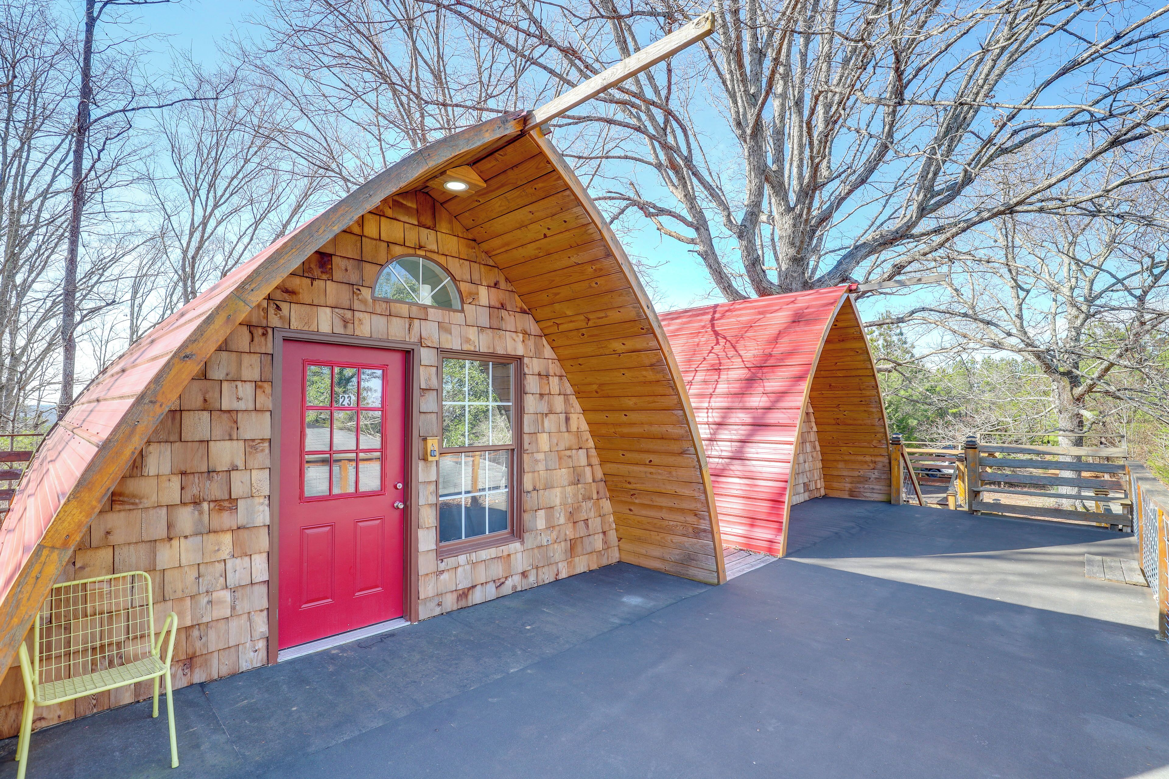 Eine Holzhütte mit roter Tür und kleinem Fenster, umgeben von Bäumen.