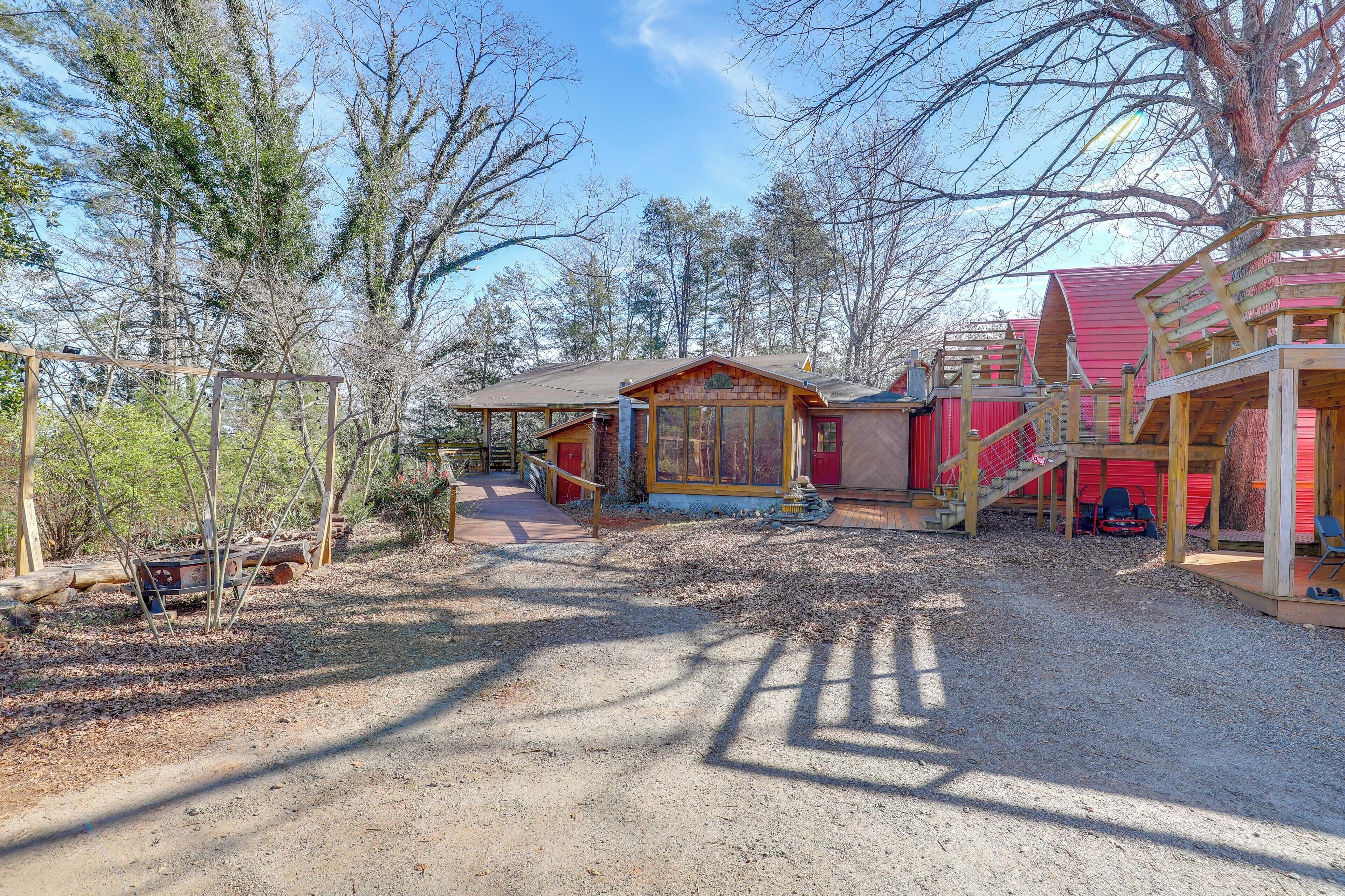 A rustic cabin with a wooden deck, a covered porch, and a red-roofed structure.