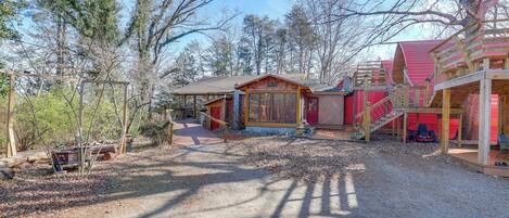 A rustic cabin with a wooden deck, a covered porch, and a red-roofed structure.